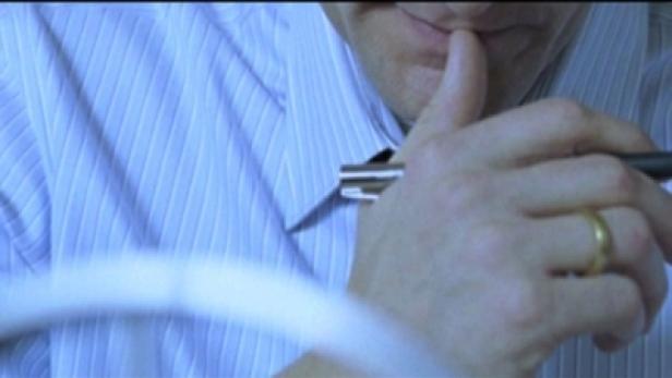 Ein Mann hält einen Stift an seine Lippen, während er nachdenklich wirkt.