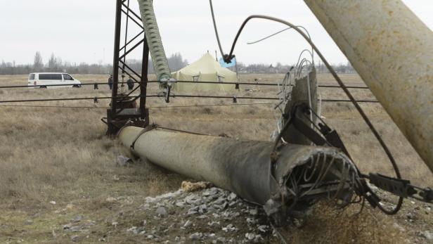 Ein zerstörter Strommast liegt in einem Feld, im Hintergrund ein Zelt und ein Lieferwagen.
