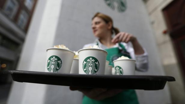 Eine Starbucks-Mitarbeiterin trägt ein Tablett mit mehreren Kaffeegetränken.