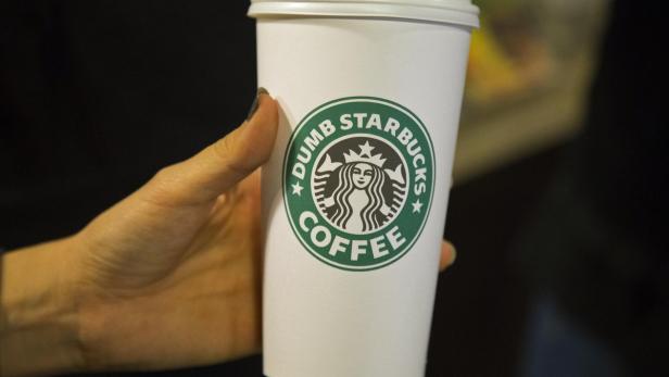 Eine Hand hält einen Kaffeebecher mit dem Aufdruck „Dumb Starbucks Coffee“.