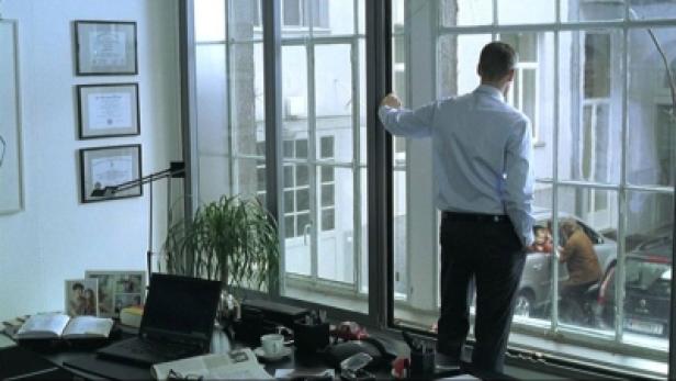 Ein Mann steht am Fenster und blickt auf die Straße.