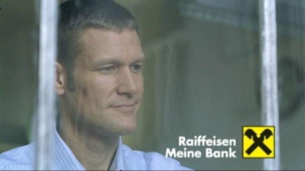 Ein Mann blickt aus dem Fenster, im Vordergrund das Logo der Raiffeisenbank.