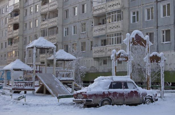 Ein verschneiter Spielplatz und ein Auto vor einem Wohnhaus im Winter.