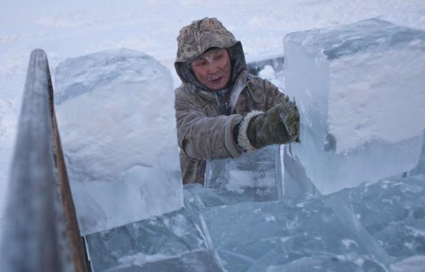Ein Mann in Winterkleidung hantiert mit großen Eisblöcken.