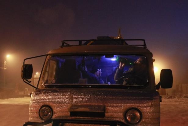 Ein Mann trinkt in der Nacht in einem gelblichen Lieferwagen eine Flasche.