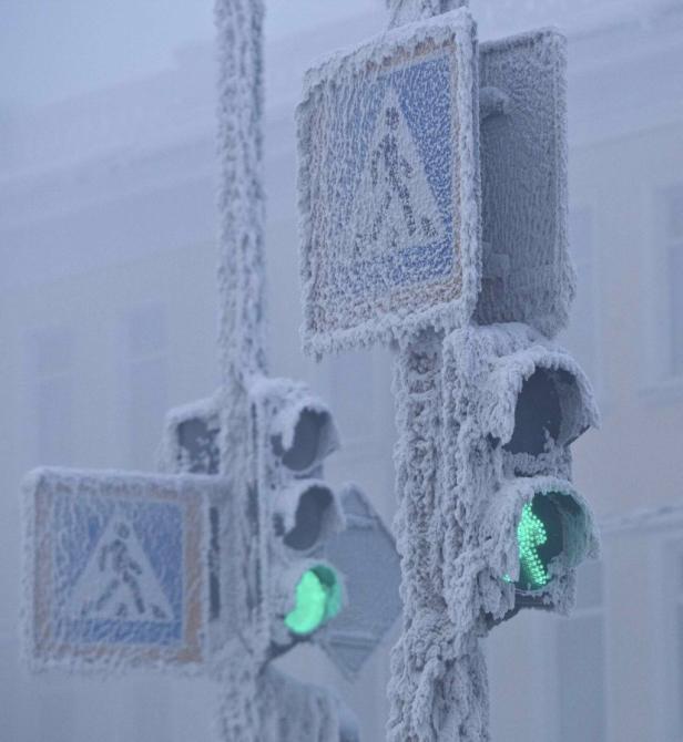 Ein Fußgängerüberweg und eine Ampel sind mit einer dicken Schicht Frost bedeckt, die Ampel zeigt Grün.