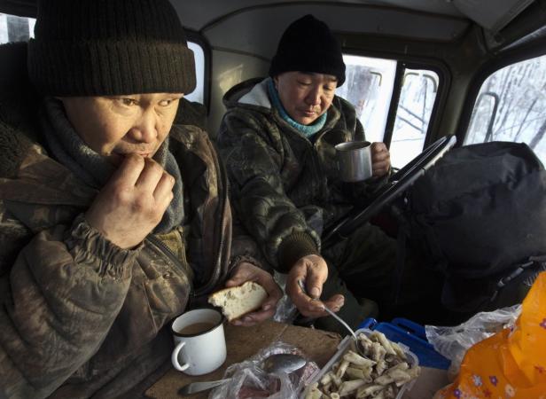 Zwei Männer in Mützen essen und trinken in der Fahrerkabine eines Lastwagens.