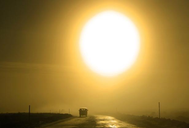 Ein Auto fährt auf einer Straße dem hellen Sonnenlicht entgegen.
