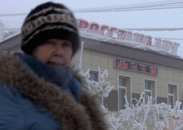 Eine Frau in Winterkleidung vor einem Gebäude mit einer Temperaturanzeige von -45 Grad Celsius.