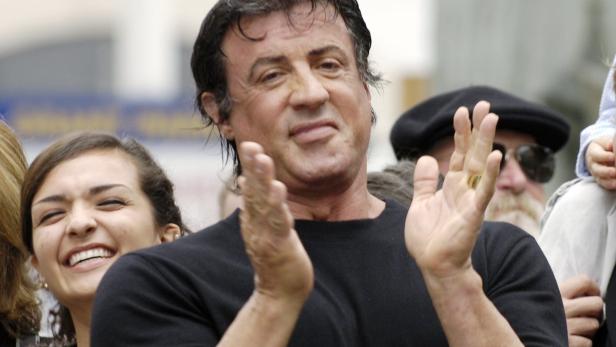 Sylvester Stallone klatscht in die Hände, umgeben von anderen Personen.