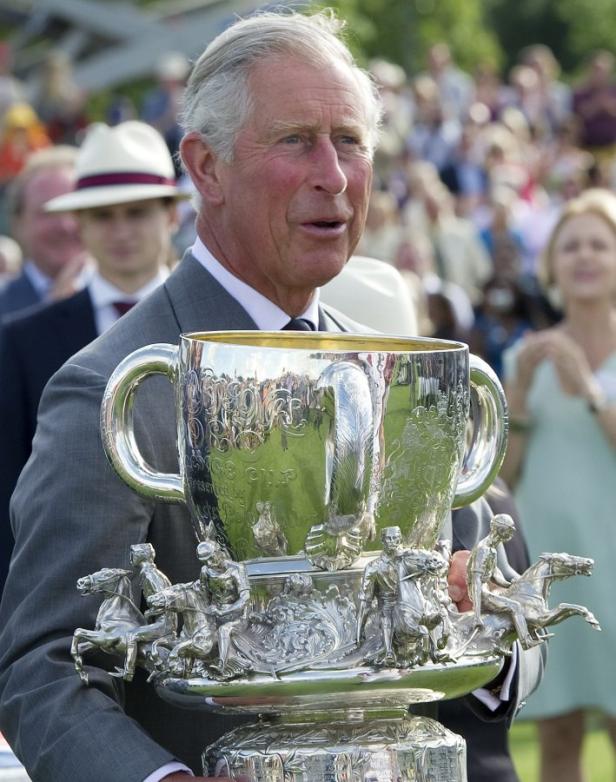 König Charles hält einen großen silbernen Pokal mit Polospieler-Figuren.