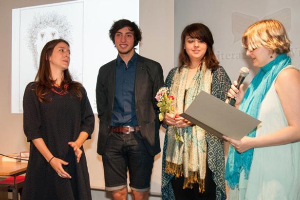 Vier Personen stehen auf einer Bühne, eine Frau spricht in ein Mikrofon.