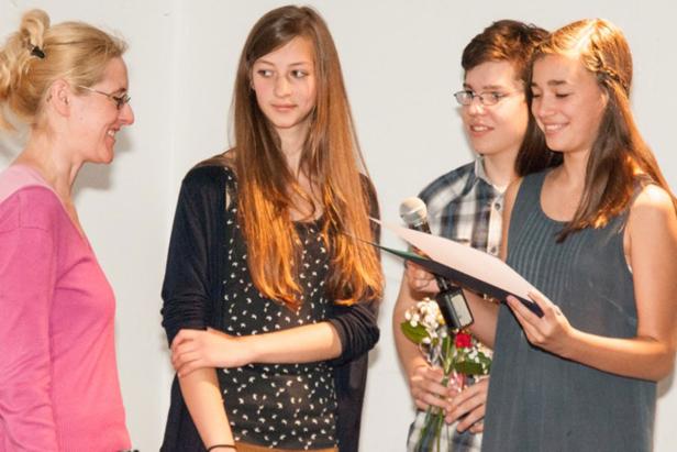 Eine Frau überreicht einer Gruppe Jugendlicher eine Auszeichnung.