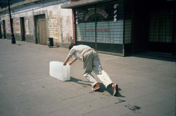 Ein Mann schiebt einen großen Eisblock auf einem Bürgersteig entlang.