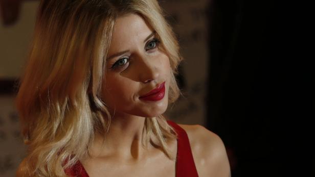 Eine Frau mit blonden, gewellten Haaren und rotem Lippenstift blickt zur Seite.