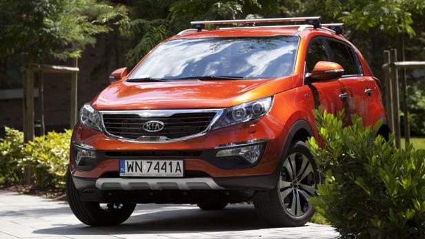 Ein orangefarbener Kia Sportage steht vor einem Haus.