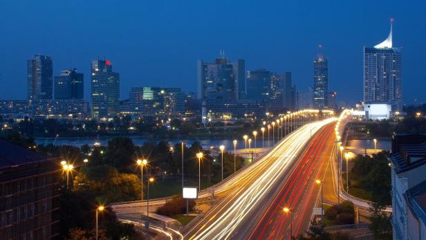 Nachts beleuchtete Skyline von Wien mit einer Brücke und viel befahrenen Straßen.