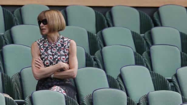 Anna Wintour sitzt mit verschränkten Armen auf einem der grünen Sitze.