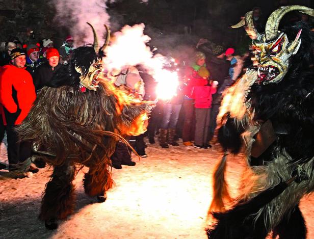 Zwei Krampusse mit furchterregenden Masken und Fackeln inmitten einer Menschenmenge.