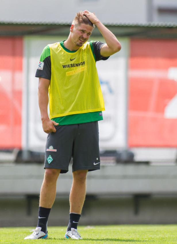 Ein Fußballspieler von Werder Bremen steht auf dem Trainingsplatz und kratzt sich am Kopf.