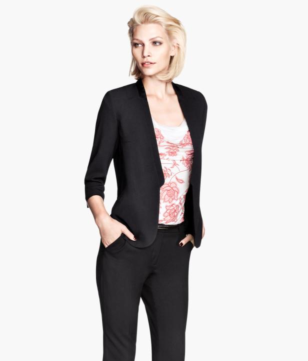 Eine blonde Frau in einem schwarzen Hosenanzug mit einem floralen Top posiert.