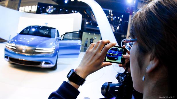 Eine Frau fotografiert mit ihrem Smartphone ein blaues Auto auf einer Automesse.