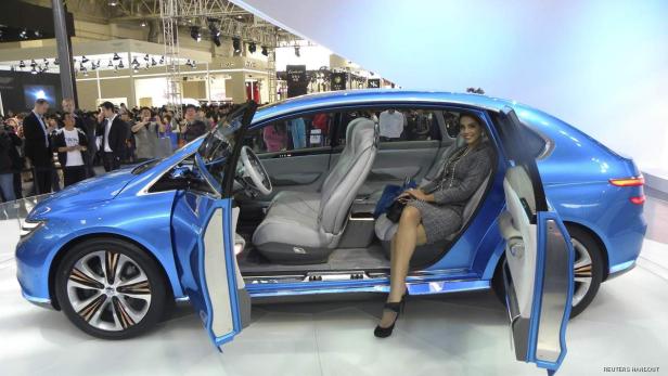 Eine Frau sitzt in einem blauen Auto mit geöffneten Türen auf einer Automesse.