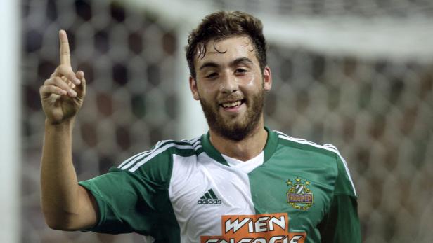 Ein lächelnder Fußballspieler von Rapid Wien zeigt mit dem Finger nach oben.