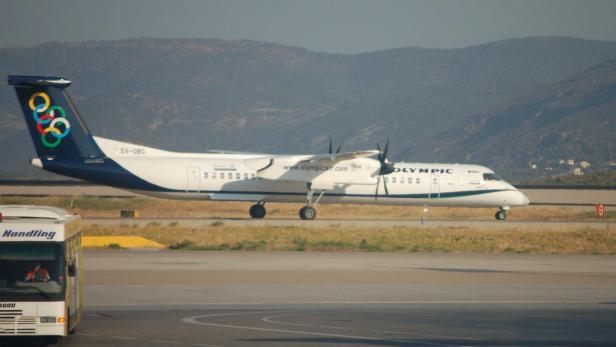 Ein Flugzeug der Olympic Air mit den olympischen Ringen auf dem Heck steht auf einem Rollfeld.