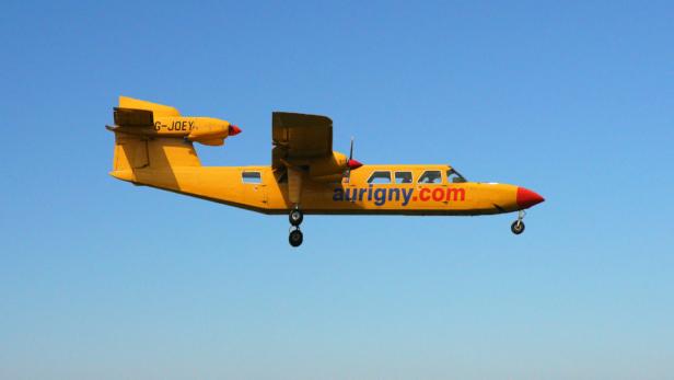 Ein gelbes Flugzeug der Fluggesellschaft Aurigny im Flug vor blauem Himmel.