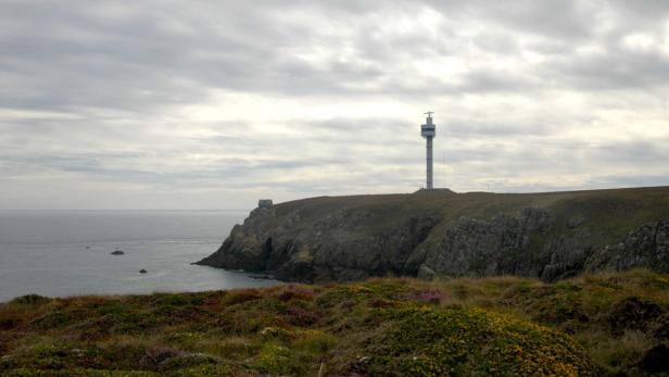 Ein Turm steht auf einer Klippe an der Küste unter bewölktem Himmel.