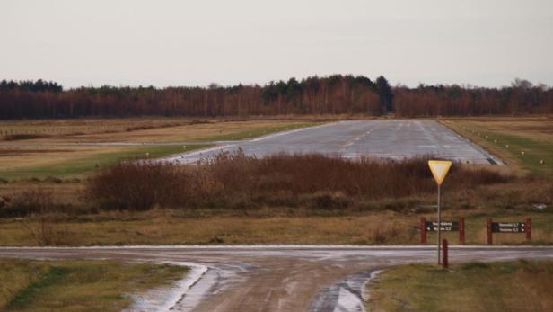 Eine Landebahn führt durch eine herbstliche Landschaft mit Bäumen im Hintergrund.