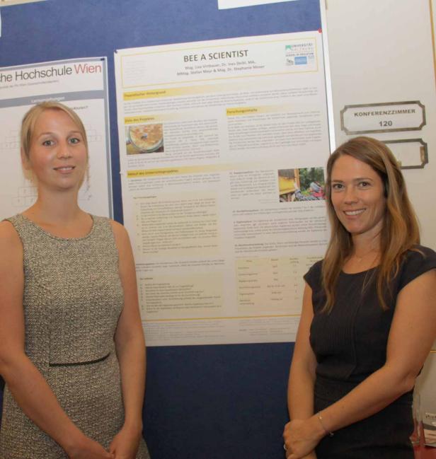 Zwei Frauen stehen vor einem Poster mit dem Titel „Bee a Scientist“.