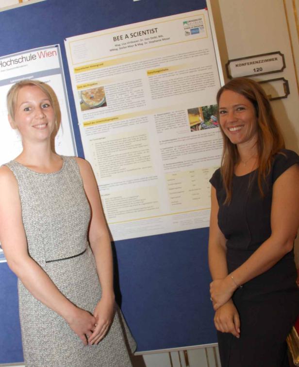 Zwei Frauen stehen vor einem Poster mit dem Titel „Bee a Scientist“.