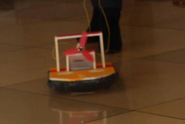 Ein selbstgebautes Hovercraft-Modell mit rotem Propeller steht auf einem gefliesten Boden.