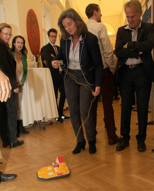 Eine Frau steuert ein Spielzeugauto mit einer Fernbedienung in einem Raum voller Menschen.