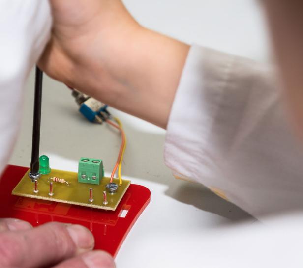 Eine Person arbeitet mit einem Schraubenzieher an einer elektronischen Schaltung.