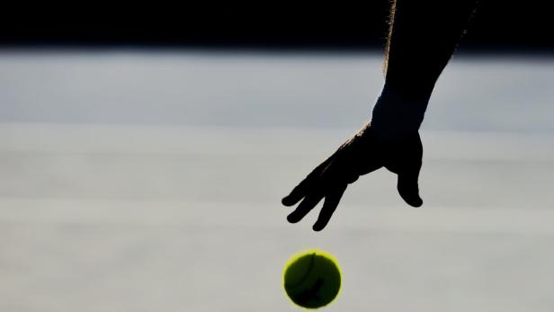 Die Silhouette einer Hand wirft einen Tennisball in die Luft.