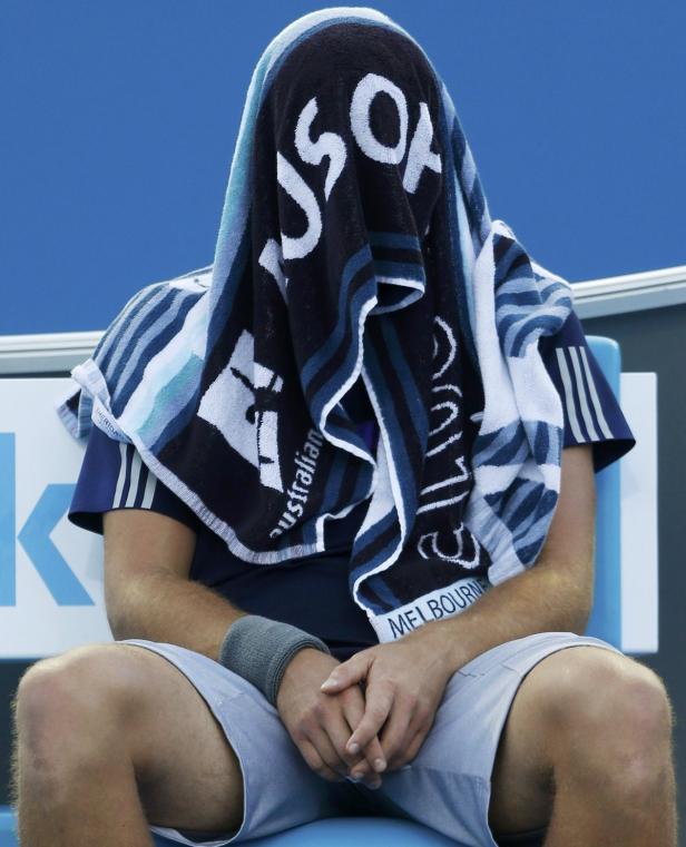 Ein Tennisspieler sitzt erschöpft mit einem Handtuch über dem Kopf auf der Bank.
