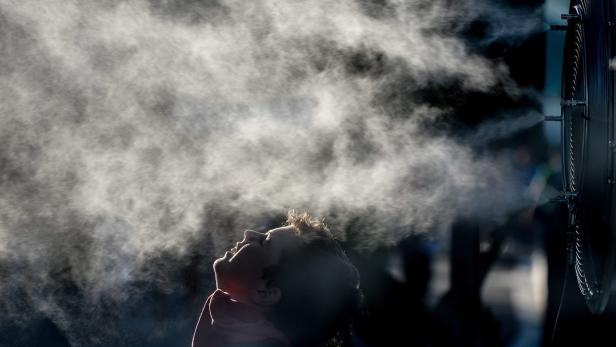 Eine Person steht unter einem kühlenden Sprühnebel eines Ventilators.