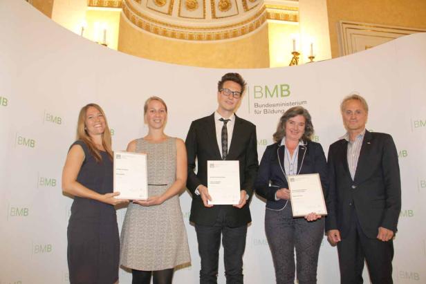 Fünf Personen posieren mit Urkunden vor einem Hintergrund des Bundesministeriums für Bildung.