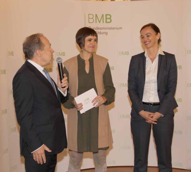 Drei Personen stehen vor einer Wand mit dem BMB-Logo.