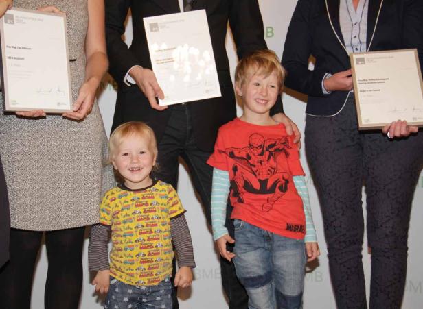 Zwei Kinder stehen mit Erwachsenen und Urkunden auf einer Bühne.