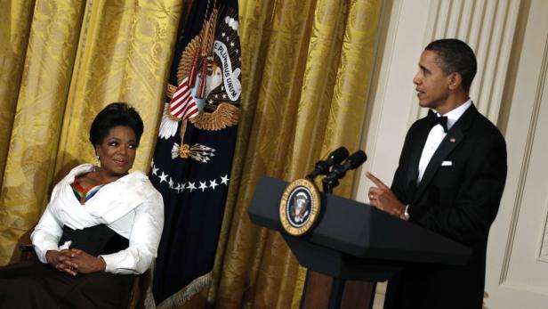 Barack Obama spricht am Rednerpult, während Oprah Winfrey daneben sitzt.