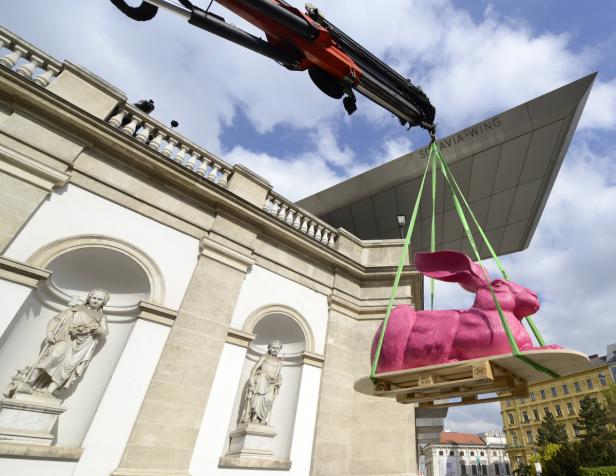 Ein Kran hebt eine große, pinkfarbene Hasenstatue vor dem Belvedere in Wien an.