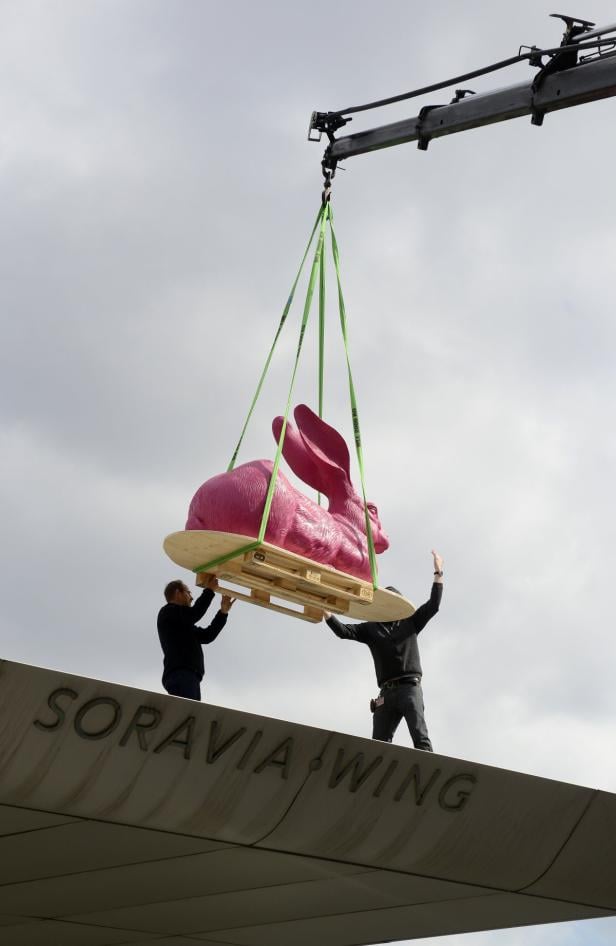 Eine pinkfarbene Hasenskulptur wird mit einem Kran auf das „Soravia Wing“-Gebäude gehoben.