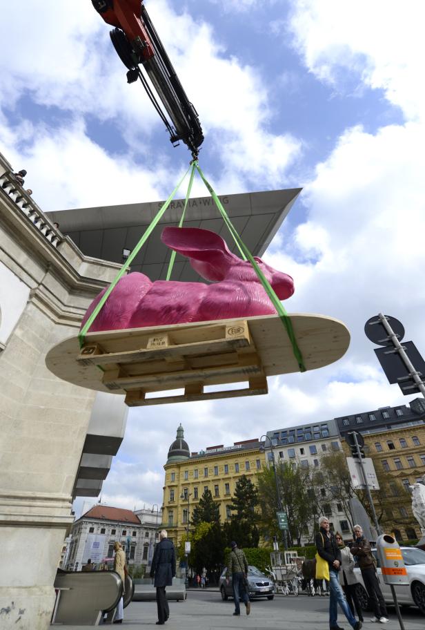 Ein Kran hebt eine große, pinkfarbene Hasenskulptur in Wien an ihren Platz.