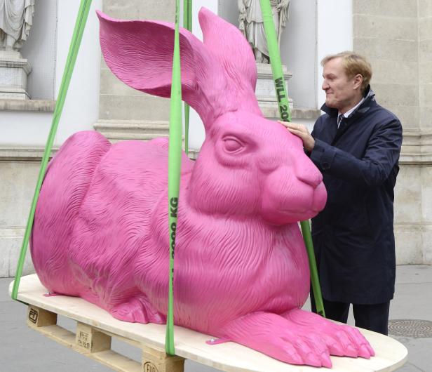Ein Mann berührt eine riesige, rosafarbene Hasenstatue, die an einem Kran hängt.