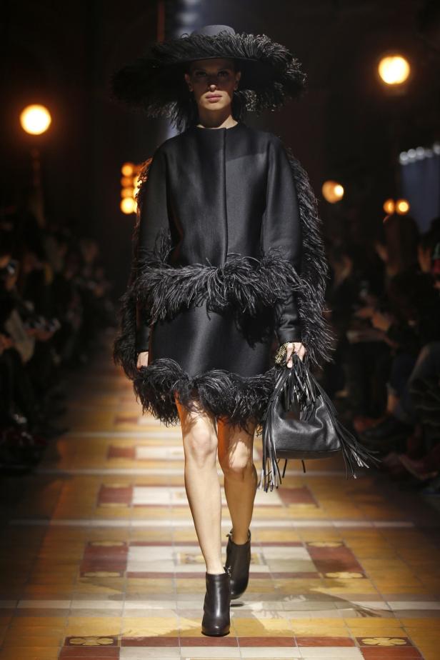 Eine Frau in einem schwarzen Federkleid und Hut auf einem Laufsteg.