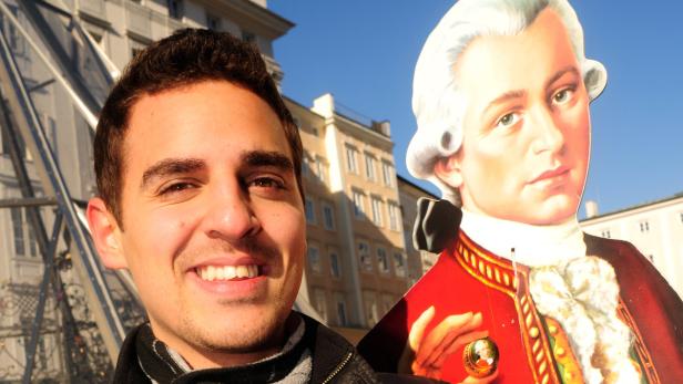 Ein lächelnder Mann posiert mit einem Pappaufsteller von Mozart in Salzburg.